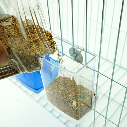 Hand filling transparent bird feeder with seeds inside cage